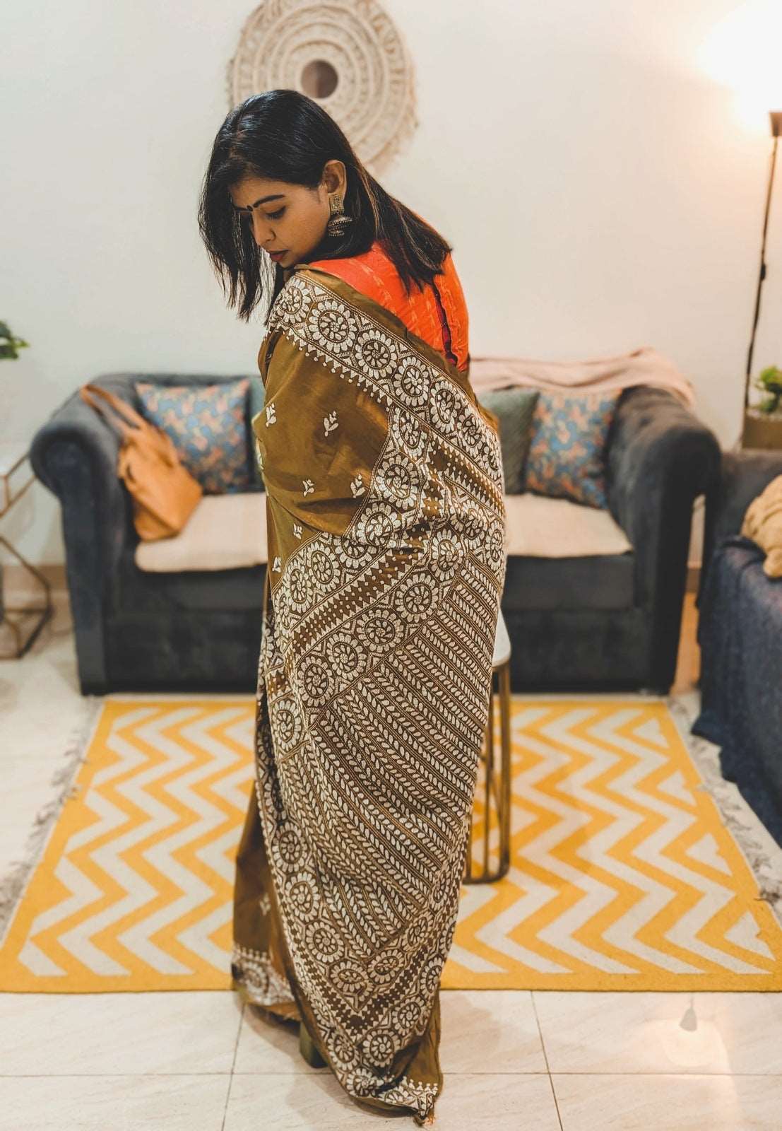 Brown silk saree with white Kantha stitch patterns and orange blouse worn by woman indoors.