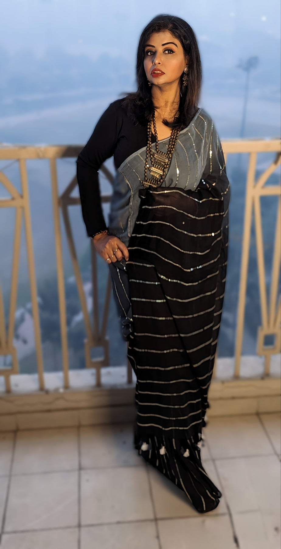 Black saree with silver horizontal stripes and tassels, paired with a black long-sleeve blouse and layered silver jewelry.