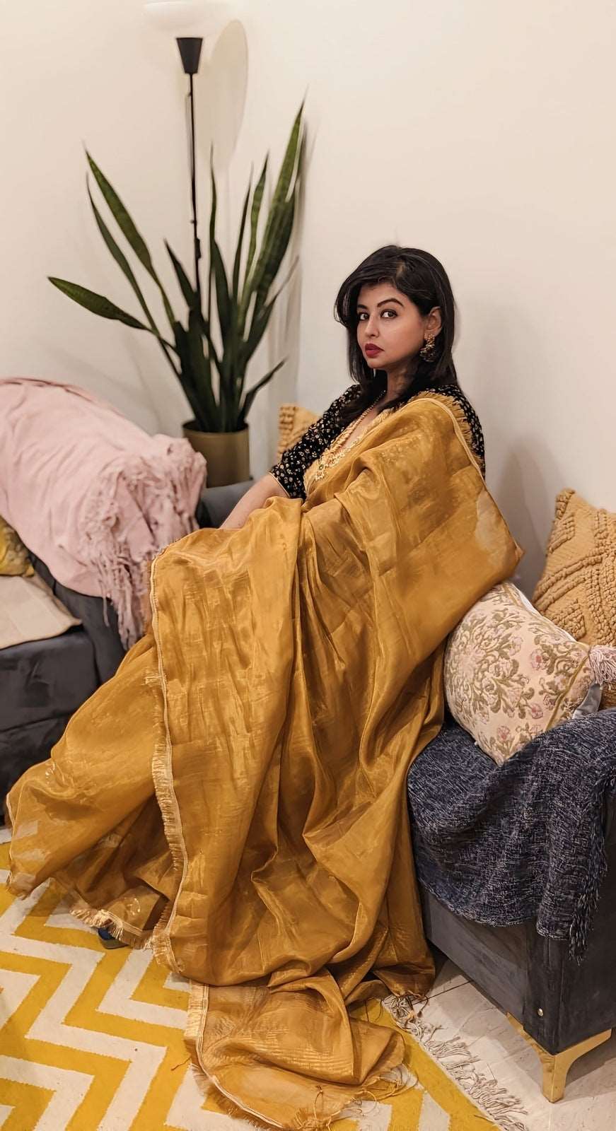 Golden silk saree with subtle shimmer worn by seated woman, paired with dark blouse and minimal jewelry.