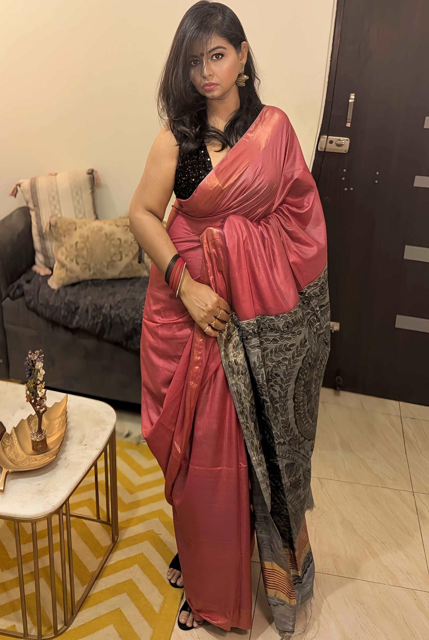 Red silk saree with intricate grey zari border draped on woman with black blouse and traditional jewelry.