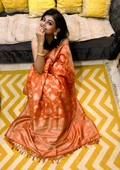 Rust orange semi Katan silk saree with gold floral motifs and zari border worn with gold earrings and bracelet.
