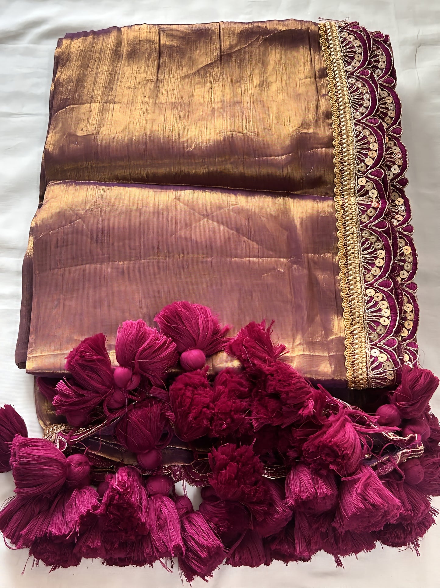 Mauve soft tissue saree with golden sheen and intricate maroon scalloped border with tassels.