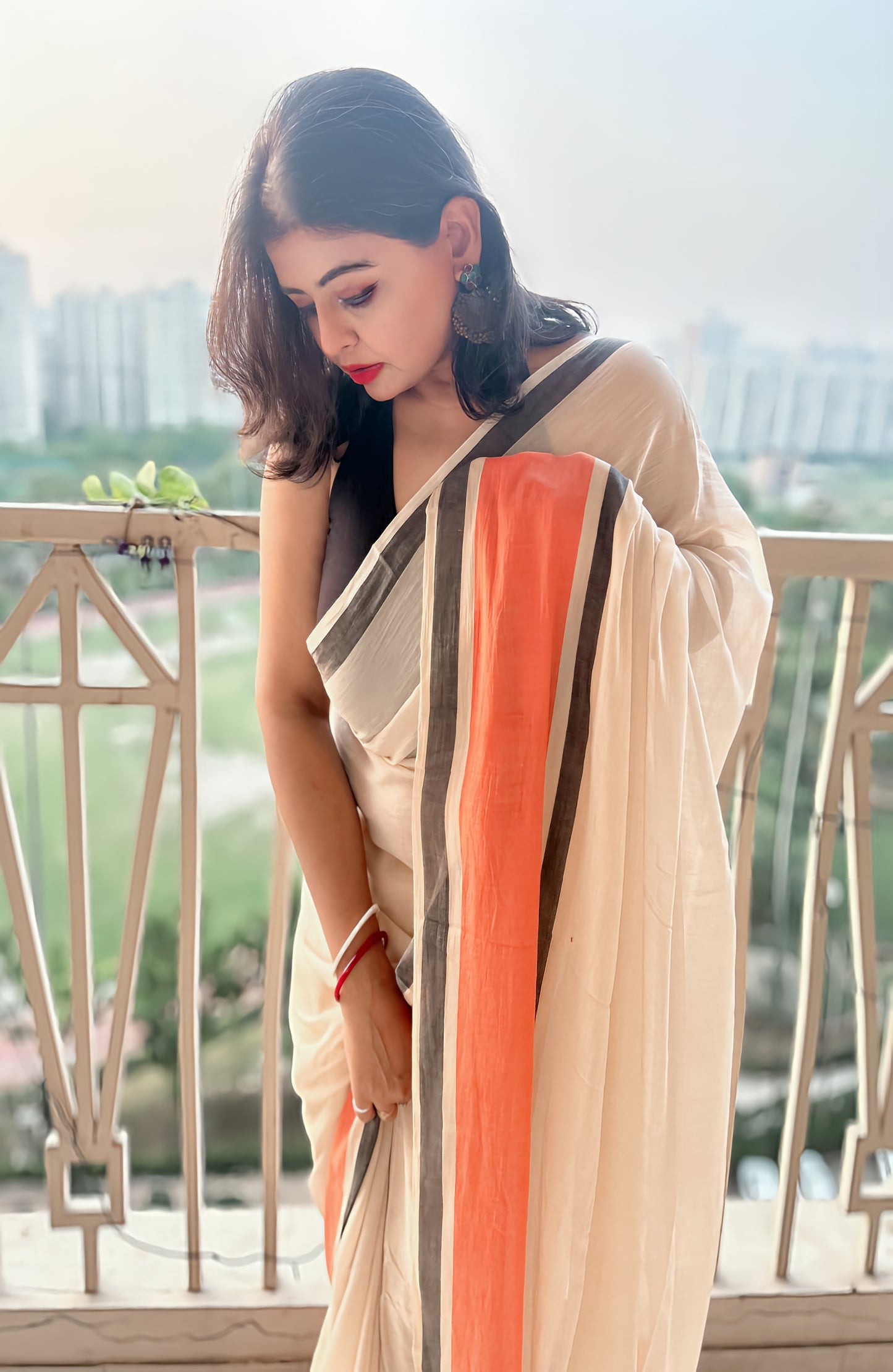 Cream handloom mul saree with bold black and orange vertical stripes and tangerine tassels.