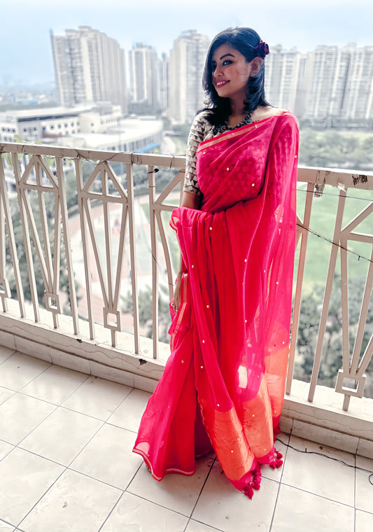 Bright pink pure handloom mul saree with gold sequin details and orange tissue crush palla worn with matching blouse.