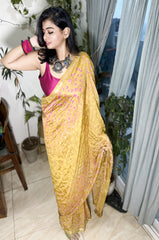 Lime green and gold bandhani saree with intricate patterns, paired with a magenta blouse and silver jewelry.