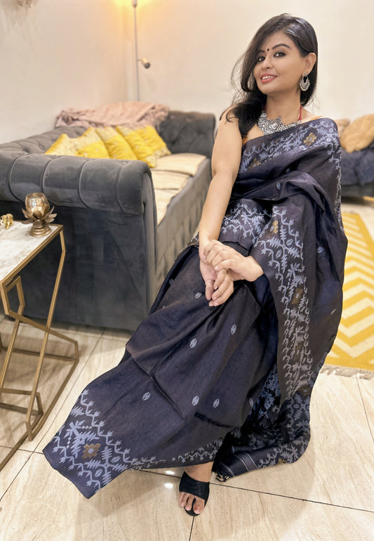 Slate blue Tussar silk Jamdani saree with intricate silver zari border and motifs, styled with sleeveless blouse.