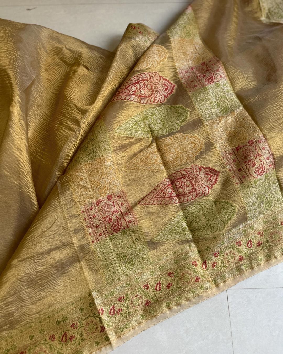 Golden glow crushed tissue saree with intricate meenakari fish motifs and floral border in red and green.