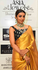 Golden yellow modal tissue saree with black blouse featuring intricate embroidery, accessorized with pearl jewelry.