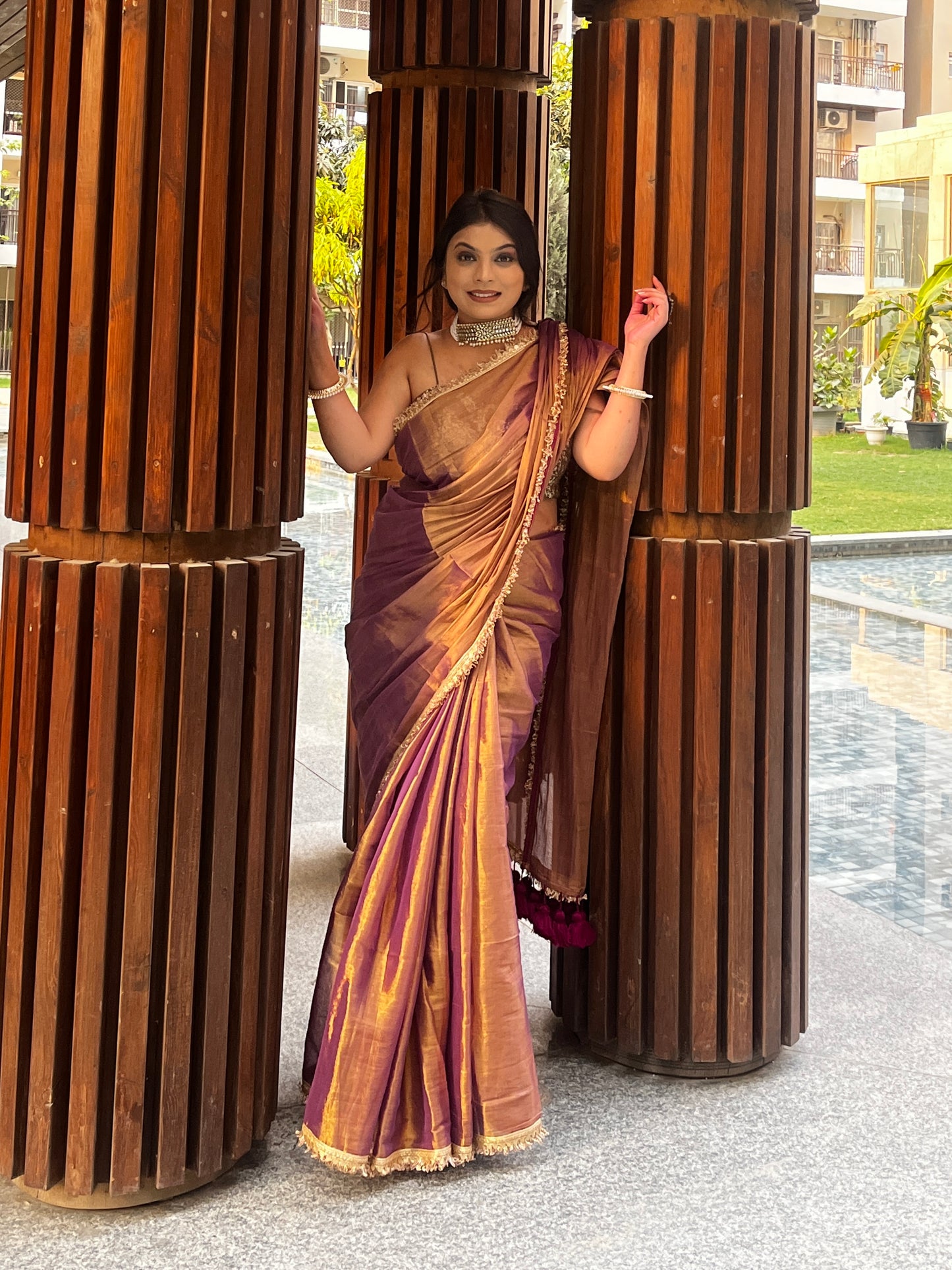 Copper purple tissue saree with gold zari border and elegant drape, worn with matching blouse.