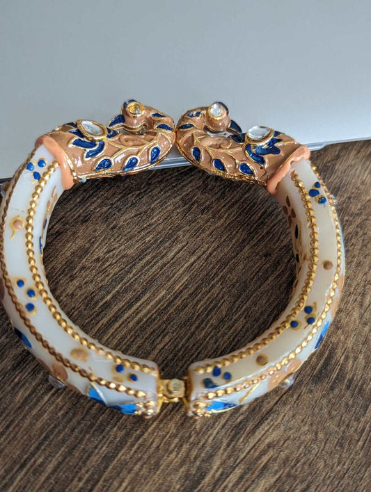 Gold-tone bangle with white enamel and blue floral peacock designs, hinged closure.