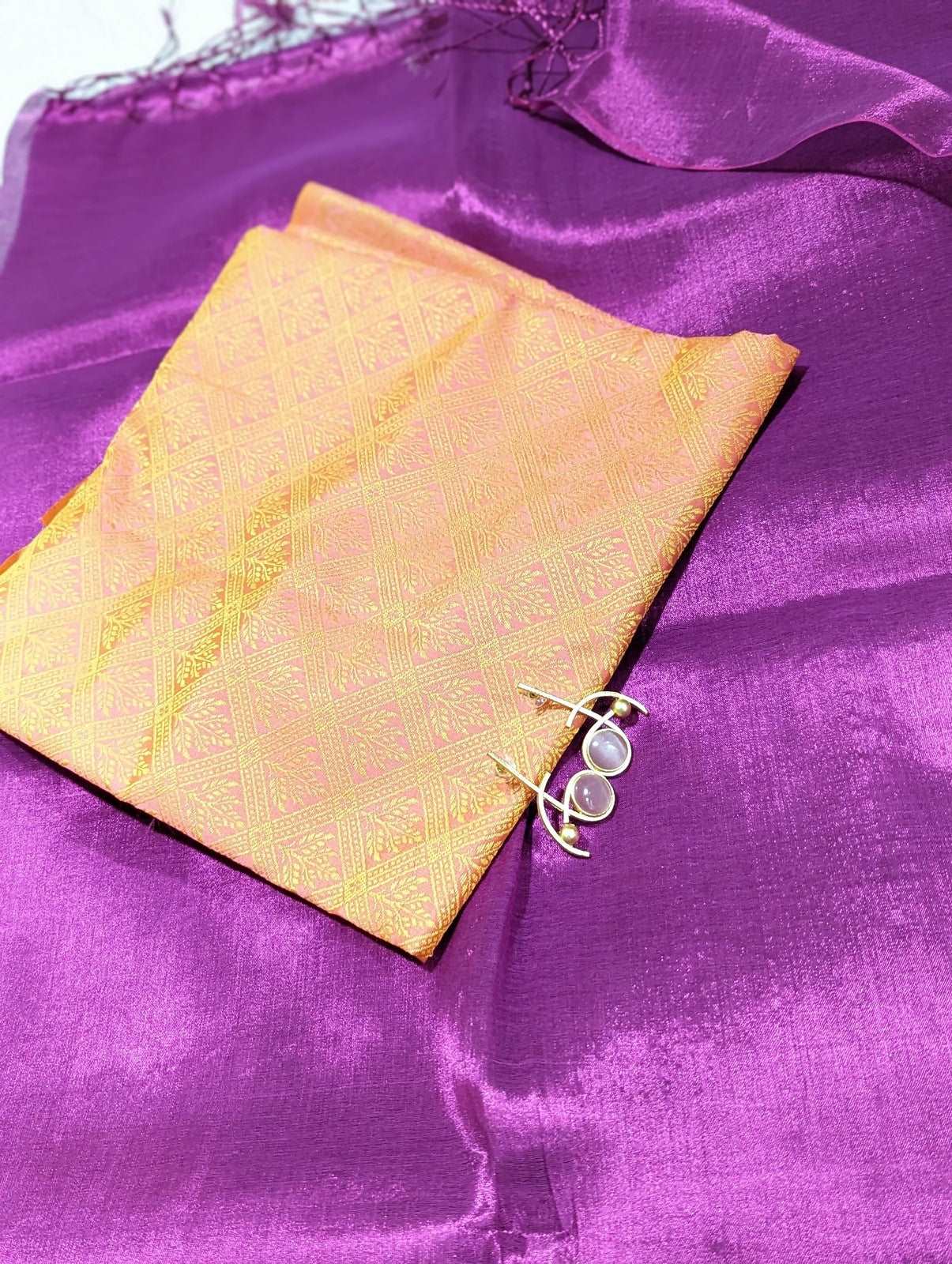 Magenta silk saree fabric with a folded golden-yellow brocade blouse piece and small silver earrings on top.