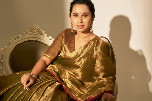 Golden soft tissue saree with shiny finish and contrasting deep red border worn by woman.