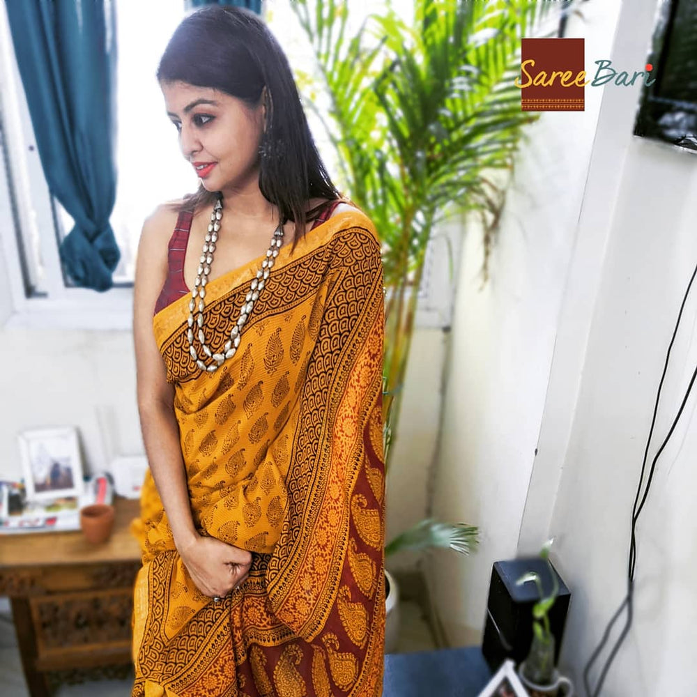 Mustard yellow Maheshwari saree with intricate floral and geometric Bagh print paired with a maroon blouse.