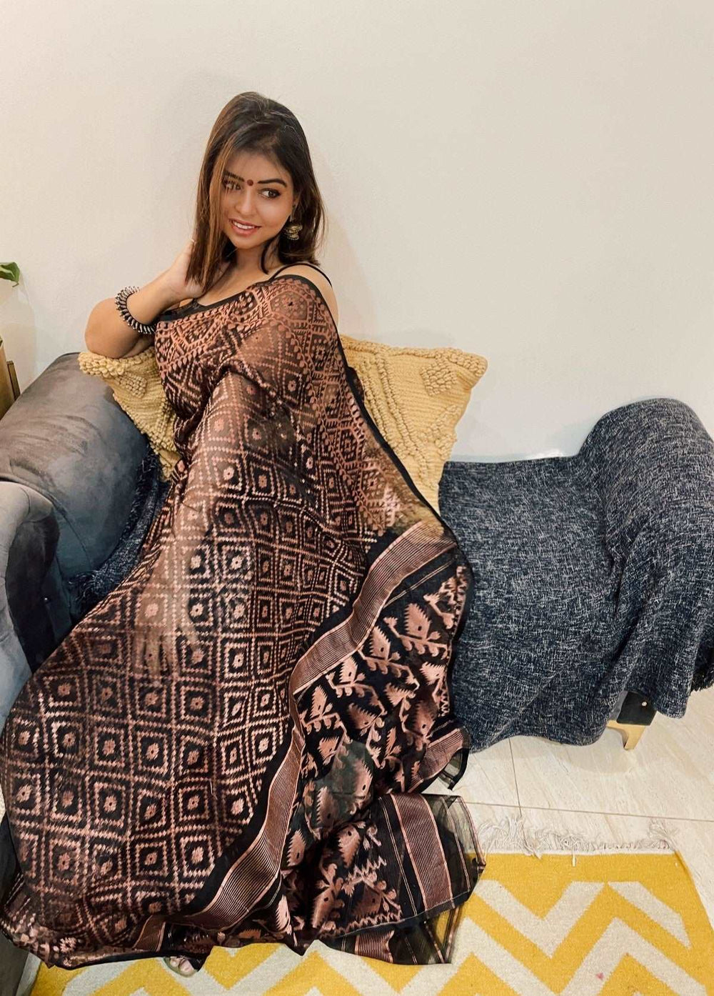 Brown and black Bengal Loom saree with geometric Dhakai Jamdani patterns worn by seated woman.