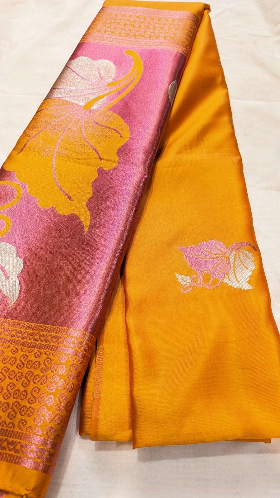 Golden yellow silk saree with pink floral and leaf motifs, traditional woven border details.