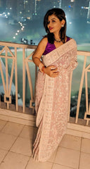 Pristine blush georgette saree with intricate thread embroidery worn with a purple blouse at night setting.