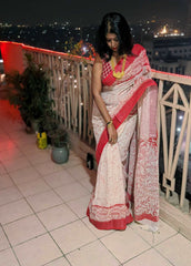 Cream and red linen cotton saree with intricate batik patterns and red border worn with traditional jewelry at night balcony .