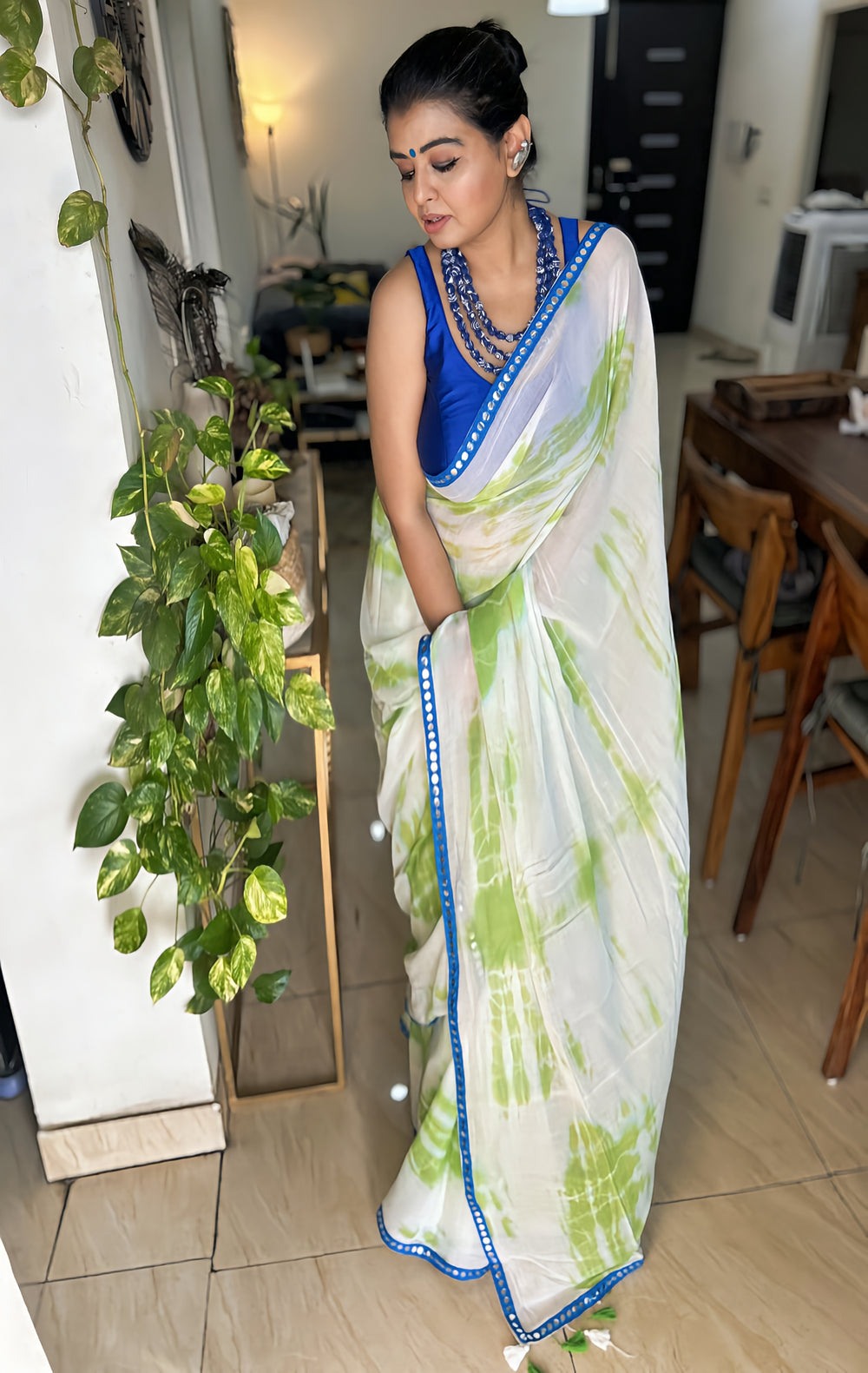 White mul cotton saree with green tie-dye patterns and blue sitara spark border worn with a blue sleeveless blouse.
