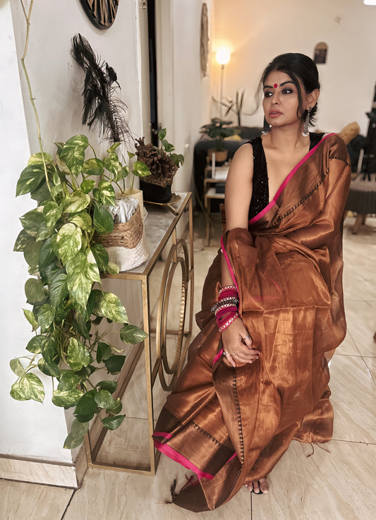 Brown silk saree with copper tones and pink border worn with black sleeveless blouse.