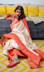Off-white silk saree with orange floral motifs and broad orange border worn with matching blouse and pink jutti shoes.