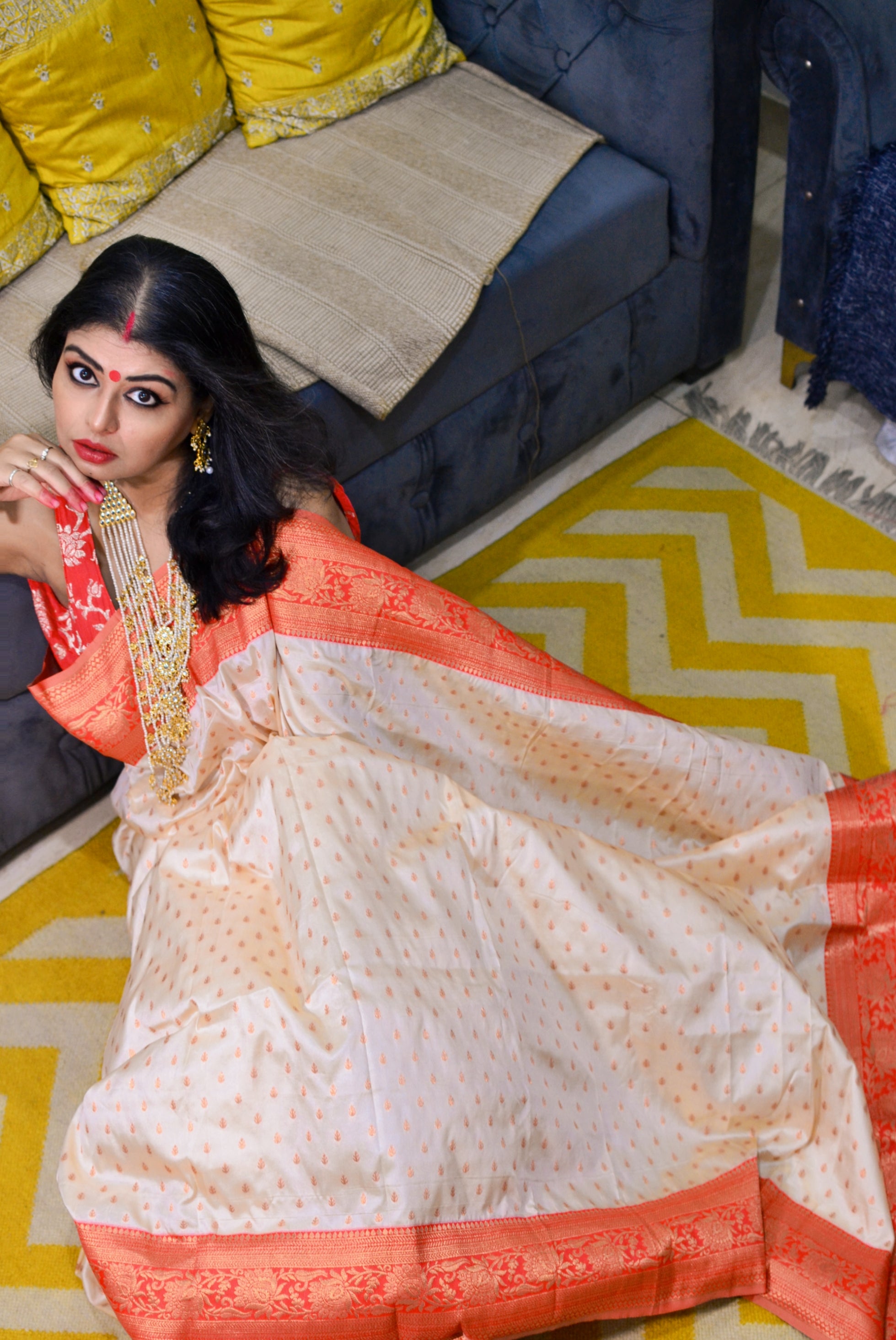 Woman in traditional outfit sitting on a yellow and white patterned rug