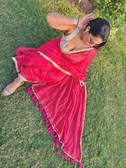 Red mul saree with tassel border paired with silver blouse worn outdoors on grass.