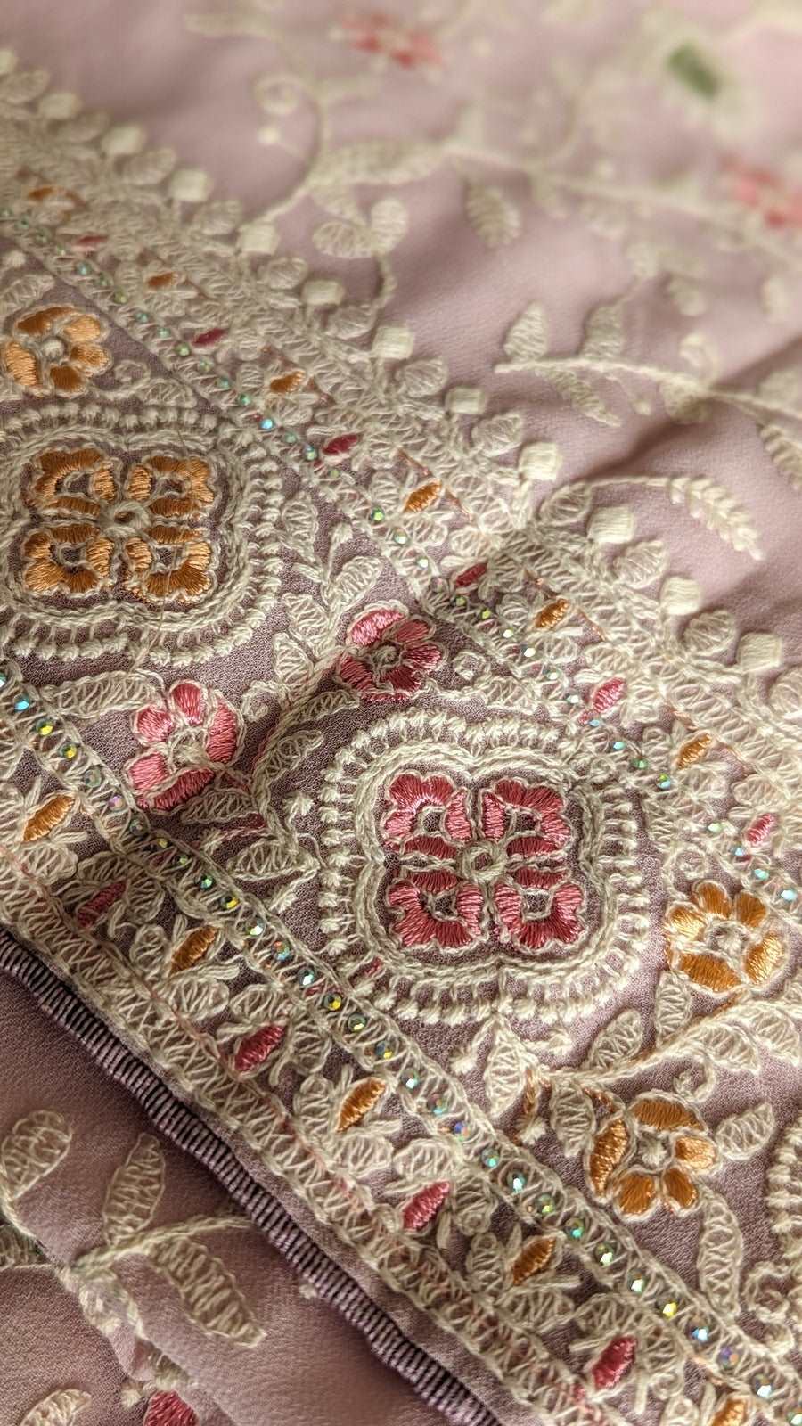 Soft blush georgette saree with intricate floral embroidery in gold, pink, and orange threads.